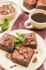 Brownie sweet chocolate dessert with walnuts and meant leaves on craft plate and cup of black coffee.