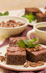 Brownie sweet chocolate dessert with walnuts and meant leaves on craft plate and cup of black coffee.