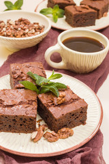 Brownie sweet chocolate dessert with walnuts and meant leaves on craft plate and cup of black coffee.