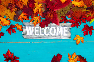Welcome sign hanging on antique teal blue wood background with colorful fall leaves border
