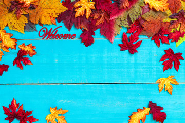 Welcome sign with color autumn leaves border hanging on antique rustic teal blue wood background; seasonal background with copy space 