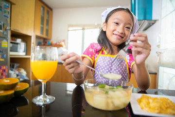 Little girl enjoy eating food with orange juice in kitchen