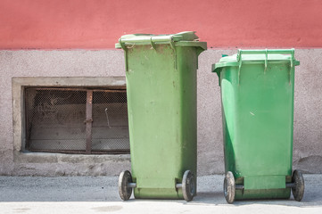 Naklejka premium Two green plastic garbage cans on the street with junk and litter waiting for dumpster truck to collect the trash