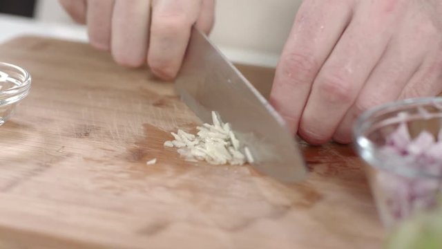 Chef mincing garlic clove with kitchen knife