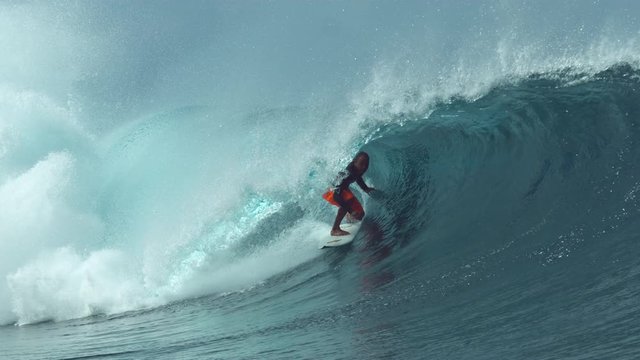SLOW MOTION, CLOSE UP: Glassy ocean water splashes over experienced surfer riding a big tube wave. Stunning shot of extreme rider challenging himself to ride the inside of a large hollow barrel wave.