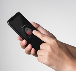 Hand holding smartphone with process of scanning fingerprint on gray background