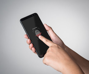 Hand holding smartphone with process of scanning fingerprint on gray background