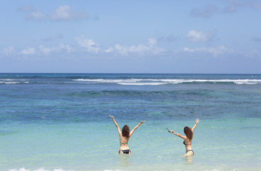 Fototapeta na wymiar Summer holidays and vacation - happy young girls sunbathing on the beach in sea having fun