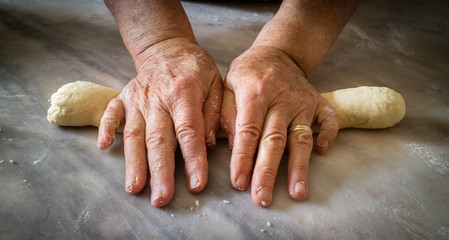 Elderly woman's hands kneading dough to make fresh bio italian pasta on marble table. Selective focus