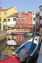 Fototapeta na wymiar Reflections of colourful houses in a canal in Burano Island , Venice,Veneto, Italy with bridge and boats