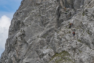 Two unrecognizable climbers facing the majestic south face of Zuc della Guardia, a mountaina in the Carnian Alps