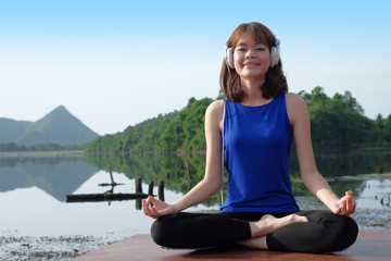 Young asian woman wear headphone and practicing yoga outdoors nature background