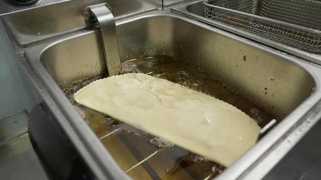 CHEBUREK fried in hot OIL &mdash; TRADITIONAL MEAT PASTRY cooking in deep fryer at food service kitchen