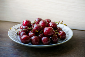 Fresh tasty cherry fruit on a plate on a wooden table. Beautiful juicy berries on a white plate.