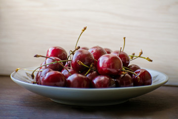 Fresh tasty cherry fruit on a plate on a wooden table. Beautiful juicy berries on a white plate.
