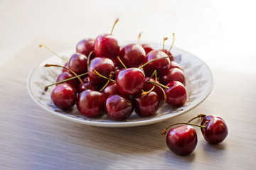 Fresh tasty cherry fruit on a plate on a wooden table. Beautiful juicy berries on a white plate.