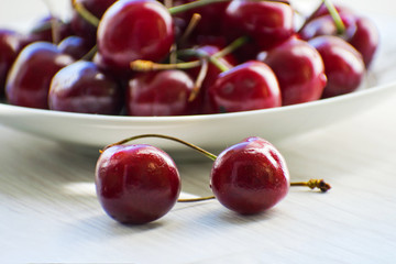 Fresh tasty cherry fruit on a plate on a wooden table. Beautiful juicy berries on a white plate.