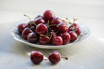 Fresh tasty cherry fruit on a plate on a wooden table. Beautiful juicy berries on a white plate.
