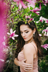 Naklejka premium Portrait of young beautiful woman with long curly hair between pink magnolia tree