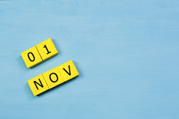 NOV 1, yellow cube calendar on blue wooden surface with copy space