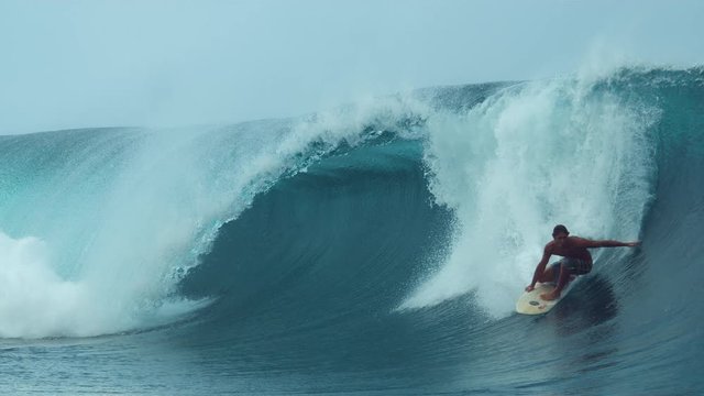 SLOW MOTION, CLOSE UP: Cheerful young male surfboarder drags his hand along the barrel wave he is riding in beautiful French Polynesia. Man enjoying an awesome summer day surfing epic ocean waves.
