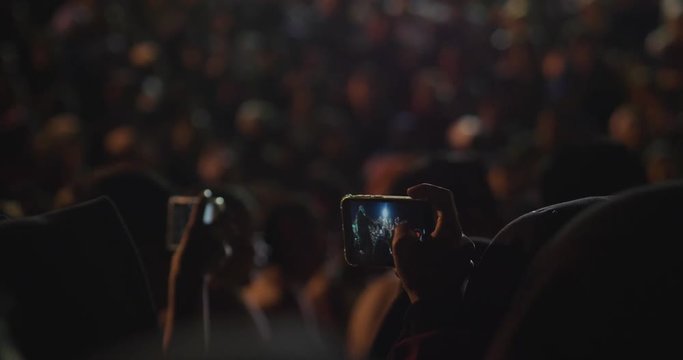 Close-up of a hand taking a picture at a concert with thousands of people having fun. Concept of: party, social network, technology, concerts...