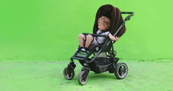 Portrait of adorable a child in a stroller on the street on green screen to be keyed or composited