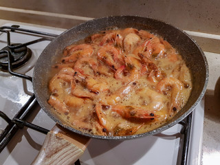 Giant orange shrimps with heads fried in oil in a frying pan on a gas stove
