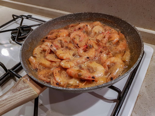 Giant orange shrimps with heads fried in oil in a frying pan on a gas stove
