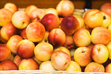 Fresh large peaches lie in a wicker basket on the counter of a small fruit market. 