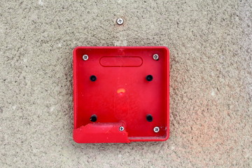 Completely broken red fire alarm plastic box switch mounted with screws on outer building wall