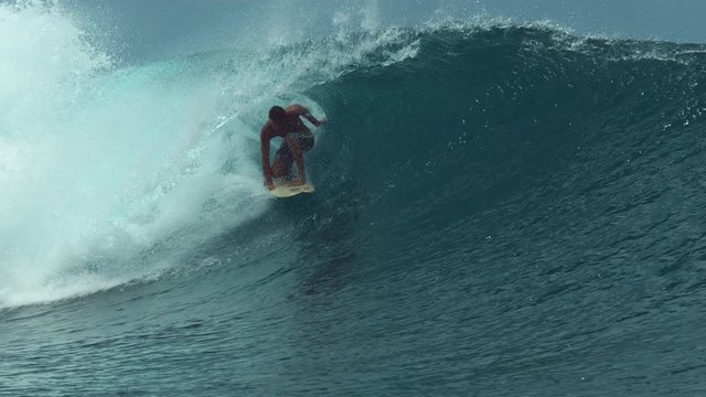 SLOW MOTION, CLOSE UP: Wild ocean wave curls over the pro surfboarder enjoying the summer in Tahiti. Spectacular view of sportsman surfing a big barrel wave splashing around the beautiful seaside.