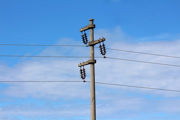 Concrete electrical power line utility pole with three connected wires on blue cloudy sky background