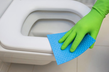 Woman in green rubber gloves cleaning toilet with blue cloth