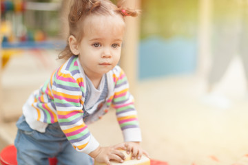 Fototapeta premium A little girl with two tails in a striped blouse plays a summer sunny day in the playground