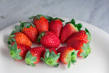 Fresh Strawberries in the white plate made of porcelain on the grey table background