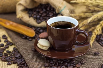 Crédence de cuisine en verre imprimé Café Hot coffee in brown cup with beans, saucer and macarons on hemp sack