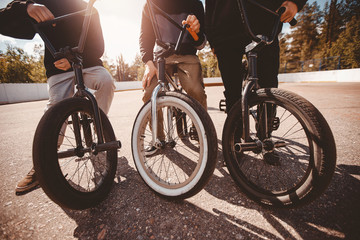 Group of teenage friends are riding bicycles bmx, doing tricks in park. Sunset light. Concept of...