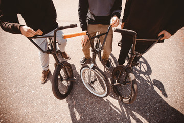 Group of teenage friends are riding bicycles bmx, doing tricks in park. Sunset light. Concept of...