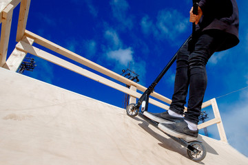 Man riding kick scooter in park ramp and springboards. Background Blue sky