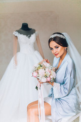 Naklejka premium Beautiful happy brunette bride in a stylish robe posing near manequin wedding dress, morning wedding preparation concept, bride portrait face closeup.