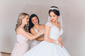 Bride preparation before wedding ceremony.  Pleasant young bridesmaids helping the bride to get ready