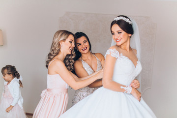 Bride preparation before wedding ceremony.  Pleasant young bridesmaids helping the bride to get ready