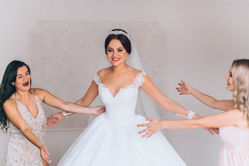 Happy bridesmaid hugging the bride in the bedroom in the morning. Before wedding ceremony. Bride...