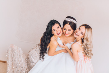 Happy bridesmaid hugging the bride in the bedroom in the morning. Before wedding ceremony. Bride preparing and wait groom. 