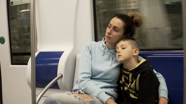 Mother and son traveling by subway train. Tired and sleepy boy lying on moms lap, woman stroking his head