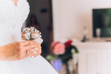 Attractive young bride before wedding ceremony holding the groom's buttonhole. flowers with pink roses, white carnation. Bride's Preparations. Wedding Morning.