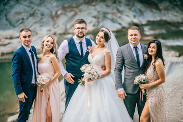 Wedding day bride and groom with bridesmaids and groomsmen posing in sunlight evening in mountains...