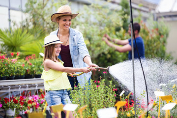 Beautiful young woman with her daughter watering the plants with a hose in the greenhouse.