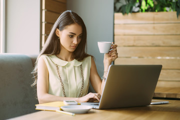 Beautiful girl working out a plan of the project and concept. Girl paints a website design on a laptop. student prints a message on the phone in the messenger. Development. Digital marketing